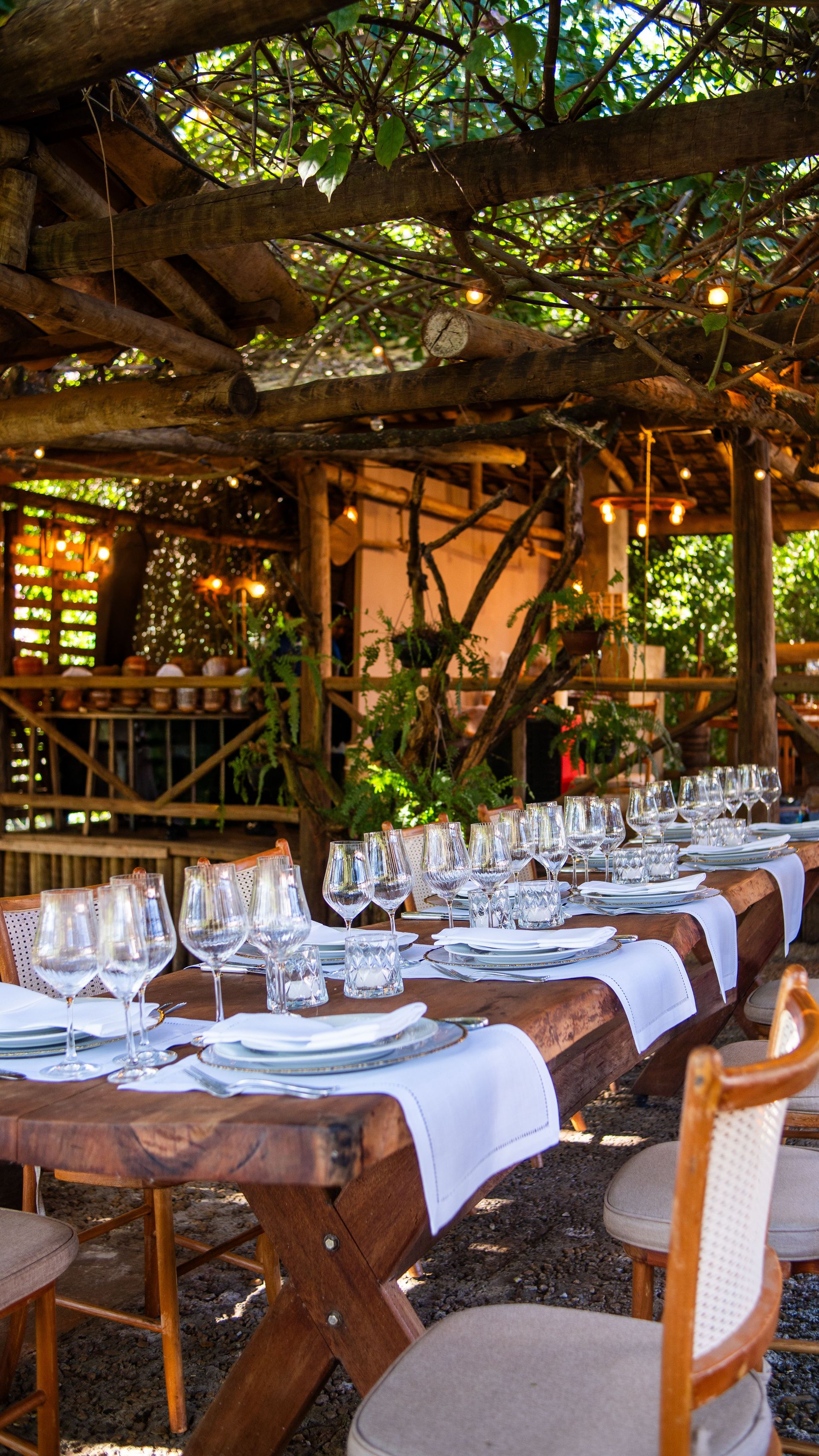 Elegant outdoor dining setup with wooden tables and chairs under a rustic canopy, perfect for events.